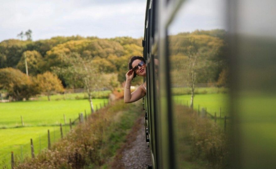 Frau schaut aus einem Zugfenster auf eine grüne Landschaft