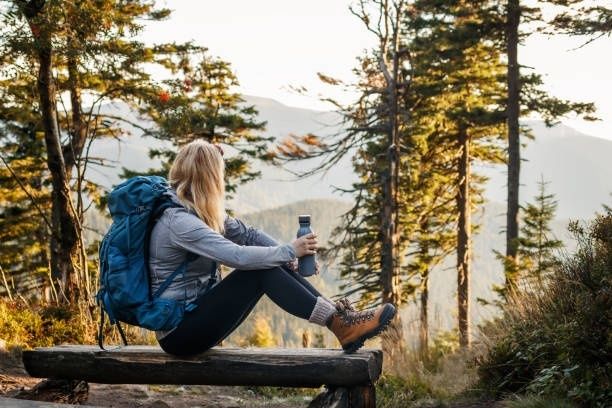Wanderin mit Rucksack ruht auf einer Holzbank im Bergwald